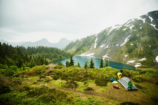 Father and son setting up tent above alpine lake during backpacking trip in rain